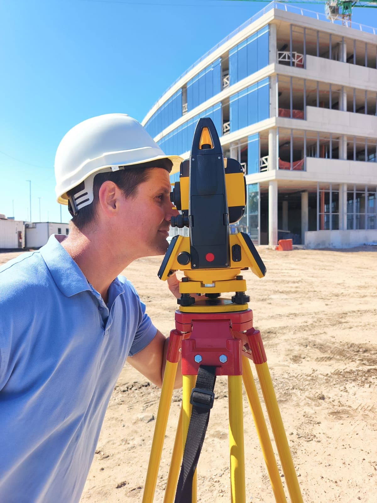 Pablo Venerus con casco realizando un relevamiento con estación total frente a un edificio en construcción